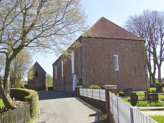 Evangelisch-reformierte Kirche Canum Backsteinkirche in Canum mit rotem Ziegeldach, Friedhof und blühenden Bäumen an einem Frühlingstag.