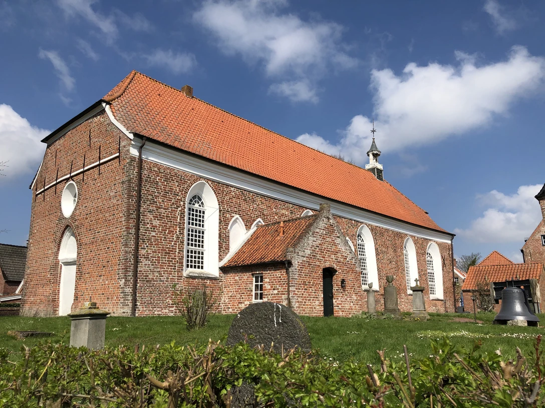 Evangelisch-reformierte Gemeinde Greetsiel Backsteinkirche mit rotem Ziegeldach und weißen Spitzbogenfenstern unter blauem Himmel.