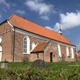 Evangelisch-reformierte Gemeinde Greetsiel Backsteinkirche mit rotem Ziegeldach und weißen Spitzbogenfenstern unter blauem Himmel.