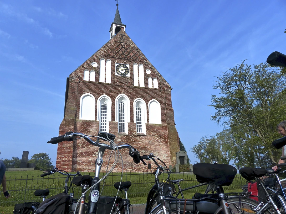 Evangelisch-reformierte Kirche Grimersum Backsteinkirche mit Uhrturm und Spitzdach, davor geparkte Fahrräder unter blauem Himmel.
