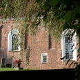 Ev.-ref. Kirche in Campen Backsteinkirche in Campen mit weißen Rundbogenfenstern, teils verdeckt von Baumzweigen.