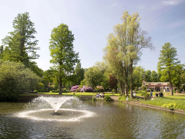 kurpark-springbrunnen Fountain in the spa gardens with water fountain, surrounded by green trees and flowering shrubs.