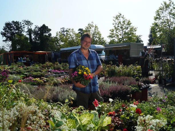 Wochenmarkt - Rhauderfehn - Ostfriesland Mann hält einen Strauß Blumen in der Hand und lächelt freundlich inmitten eines Blumenstandes.
