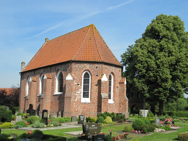 Die Kapelle in Vreschen-Bokel aus Backstein mit roten Dachziegeln, umgeben von gepflegten Gräbern und Pflanzen.