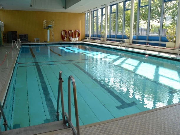 sprungbrett Schwimmbecken mit Sprungbrett unter Tageslicht, umgeben von Fenstern und Rettungsringen an der Wand.