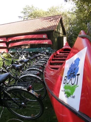 Paddel- und Pedal Rhauderfehn, Ostfriesland Rote Kanus und Fahrräder nebeneinander vor einem Holzschuppen mit rotem Ziegeldach