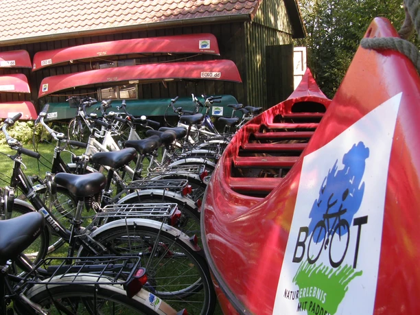 Paddel- und Pedal Rhauderfehn, Ostfriesland Rote Kanus und Fahrräder nebeneinander vor einem Holzschuppen mit rotem Ziegeldach