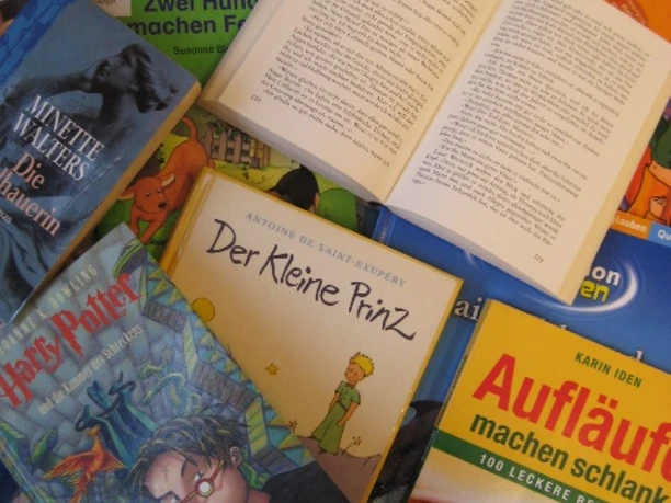 Bücher in der Bücherei IMG_3654.JPG Mehrere auf einem Tisch liegende Bücher, darunter 'Der Kleine Prinz', 'Harry Potter', 'Aufläufe machen schlank' und weitere Kinder- und Sachbücher