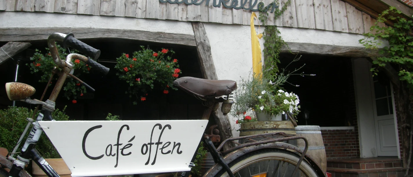 De Holter Wienkeller Fahrrad mit Schild Café offen vor Eingang zu 'De Holter Wienkeller', einem rustikalen Gebäude mit Holzfassade