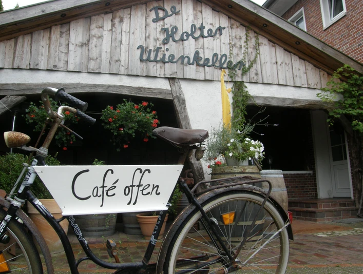 De Holter Wienkeller Fahrrad mit Schild Café offen vor Eingang zu 'De Holter Wienkeller', einem rustikalen Gebäude mit Holzfassade
