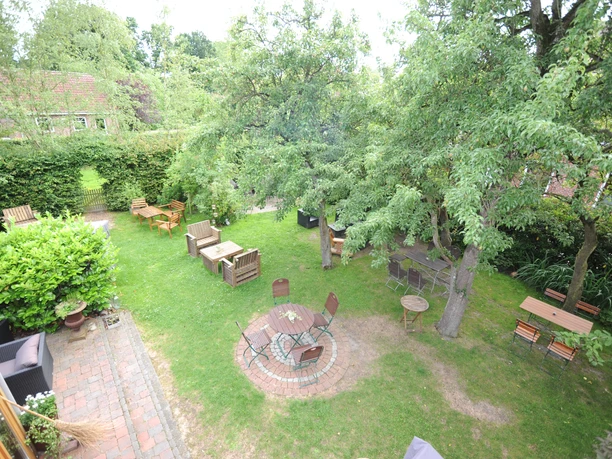 De Holter Wienkeller, Außenbereich, Erholungsort Rhauderfehn5 Garten mit mehreren Sitzbereichen aus Holzstühlen und Tischen, umgeben von Bäumen und Hecken