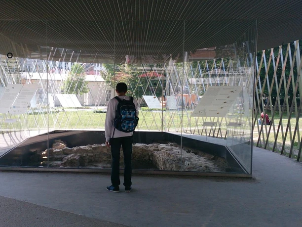 Eine Person mit Rucksack betrachtet ein archäologisches Bodendenkmal durch eine Glasvitrine.