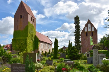 St. John's Church rises majestically above the well-tended churchyard with its flower beds and gravestones. The tower is covered in ivy, which gives it a picturesque appearance.