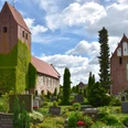 Die St.-Johannes-Kirche erhebt sich majestätisch über den gepflegten Kirchhof mit blühenden Beeten und Grabsteinen. Der Turm ist mit Efeu bewachsen, was ihm ein malerisches Aussehen verleiht.