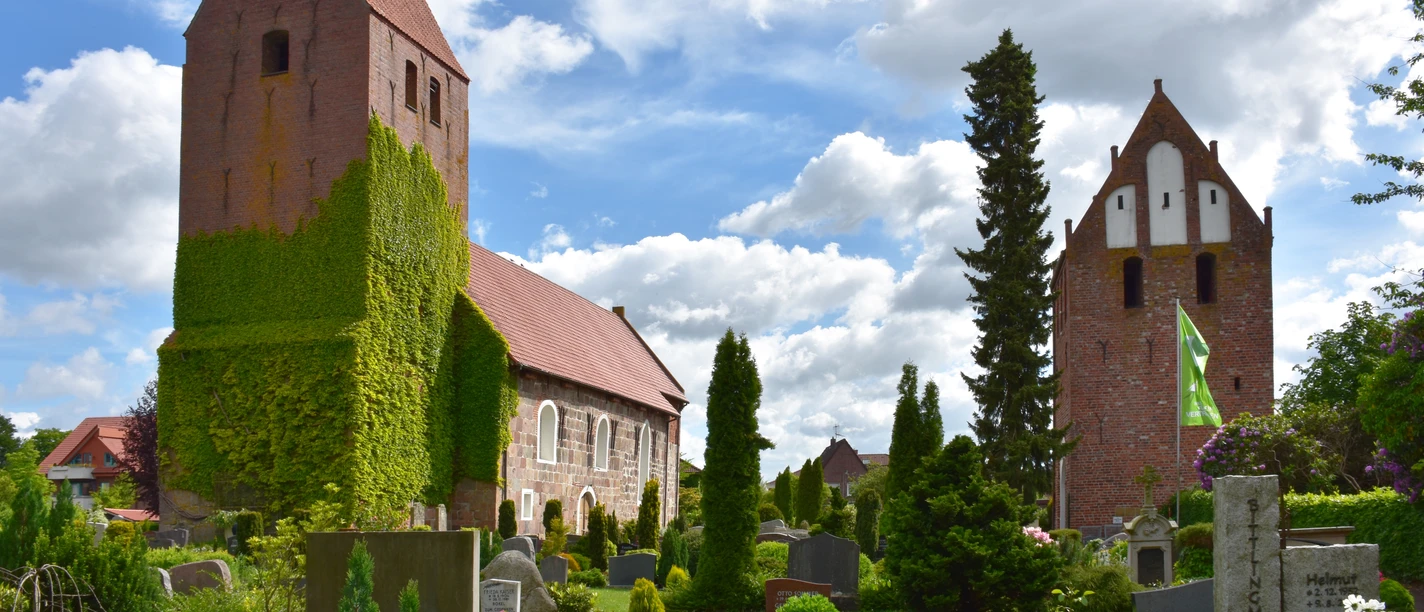 St-Johannes Kirche Die St.-Johannes-Kirche erhebt sich majestätisch über den gepflegten Kirchhof mit blühenden Beeten und Grabsteinen. Der Turm ist mit Efeu bewachsen, was ihm ein malerisches Aussehen verleiht.