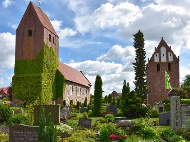 St-Johannes Kirche Die St.-Johannes-Kirche erhebt sich majestätisch über den gepflegten Kirchhof mit blühenden Beeten und Grabsteinen. Der Turm ist mit Efeu bewachsen, was ihm ein malerisches Aussehen verleiht.