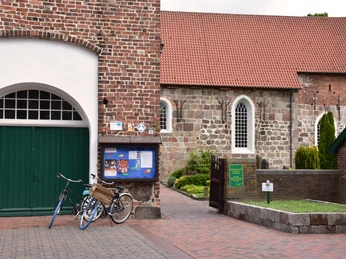 Ziegelkirche mit rotem Dach, angeschlossenem Tor und Eingangsbereich; Fahrräder lehnen an der Wand.