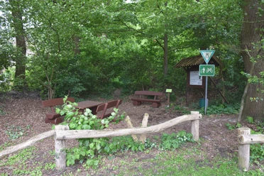 Bokeler Burg Im grünen Wald steht eine rustikale Holzgarnitur mit Tisch und Bänken nahe einem Weg; Schilder weisen auf Wanderstrecken hin.