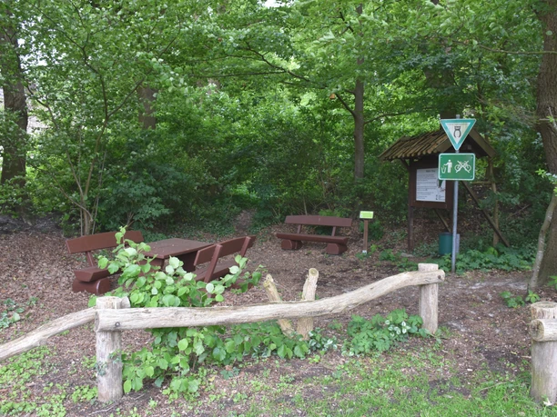 Bokeler Burg Im grünen Wald steht eine rustikale Holzgarnitur mit Tisch und Bänken nahe einem Weg; Schilder weisen auf Wanderstrecken hin.