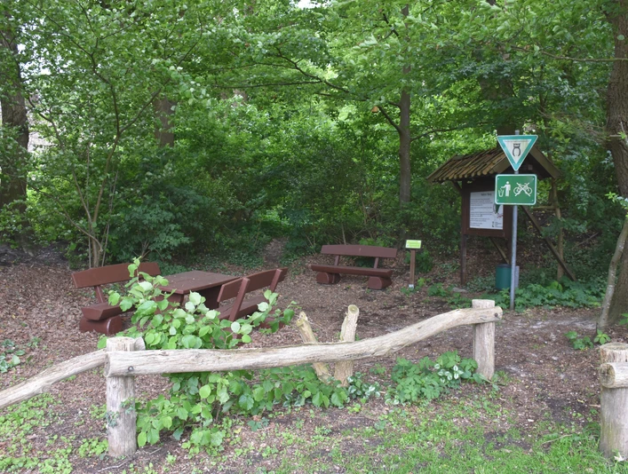 Bokeler Burg Im grünen Wald steht eine rustikale Holzgarnitur mit Tisch und Bänken nahe einem Weg; Schilder weisen auf Wanderstrecken hin.