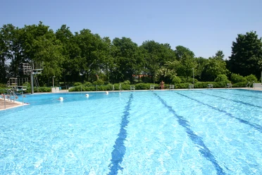 Freibad Ein großes, glitzerndes Freibad mit türkisblauem Wasser, umgeben von üppigem Grün.