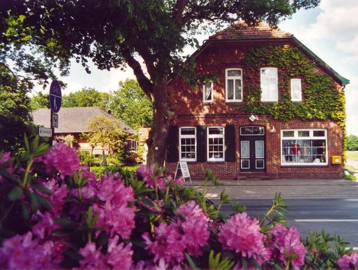 Tante Emma Laden Ein traditioneller Tante-Emma-Laden in einem Backsteinhaus, umgeben von blühendem Rhododendron.