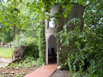 Kapelle "Unter den Linden" Eine kleine, runde Kapelle aus Stein, umgeben von Bäumen und grünem Laub.