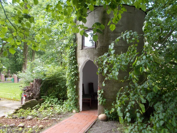 Kapelle "Unter den Linden" Eine kleine, runde Kapelle aus Stein, umgeben von Bäumen und grünem Laub.