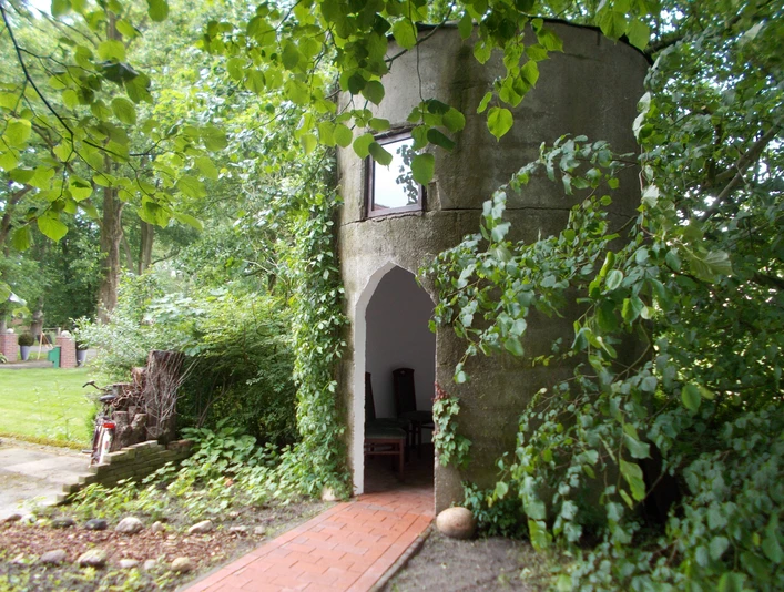 Kapelle "Unter den Linden" Eine kleine, runde Kapelle aus Stein, umgeben von Bäumen und grünem Laub.