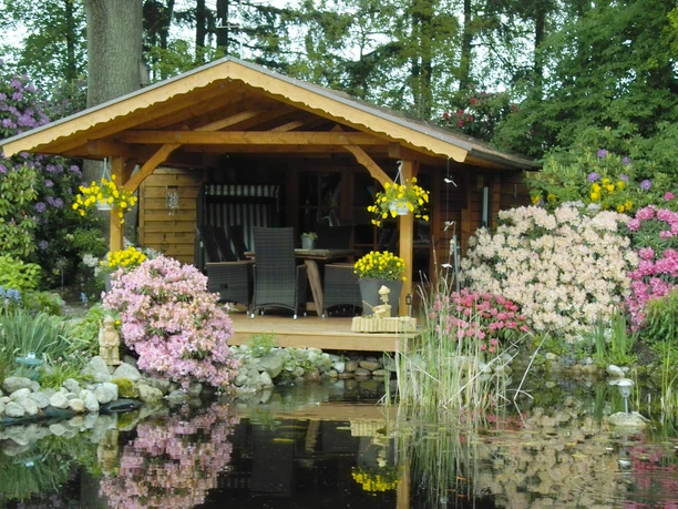 Teichanlage mit Gartenhütte Die idyllische Teichanlage mit einer gemütlichen Gartenhütte wird von blühenden Pflanzen eingerahmt.