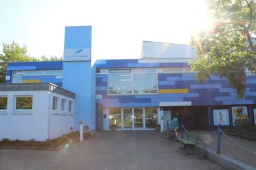 Aqua Park Hallenbad Papenburg Eingangsbereich des Aqua Park Hallenbads Papenburg mit blau-gelber Fassade bei Sonnenlicht.
