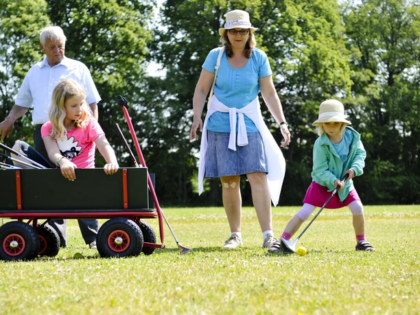 Swingolf Eine Familie spielt Swingolf auf einer grünen Wiese. Zwei Kinder schwingen Schläger, während Erwachsene zusehen.