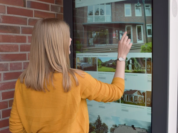 Infoterminal Eine Frau interagiert mit einem großen Infoterminal außen an einem Gebäude.
