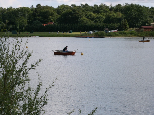 Almsee Auf dem ruhigen See paddelt ein Boot zwischen grünen Ufern und Bäumen unter einem klaren Himmel.