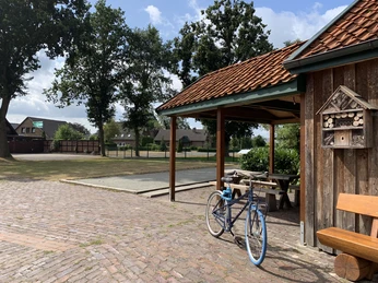 Boule Hof Kleiberg Gepflasterter Hof mit Holzgebäude, kleinem Sitzplatz, Parkbank und blauem Fahrrad. Umgeben von Bäumen und Boulefeld. Ruhiges Ambiente.