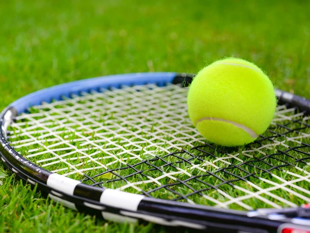 Tennis Ein Tennisschläger liegt diagonal auf grünem Rasen, daneben ein leuchtend gelber Tennisball.