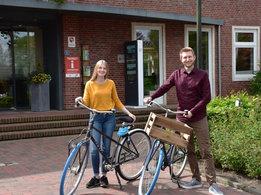 Mitarbeiter Tourist-Info Vor einem Tourist-Info-Gebäude stehen zwei lächelnde Mitarbeiter neben Fahrrädern.