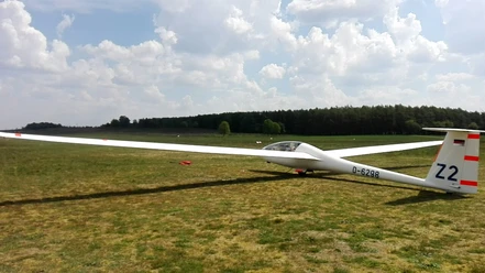 Segelfluggelände des Luftsportvereins Papenburg-Hümmling e.V. Segelflugzeug mit ausgebreiteten Flügeln auf einer grünen Wiese unter leicht bewölktem Himmel.