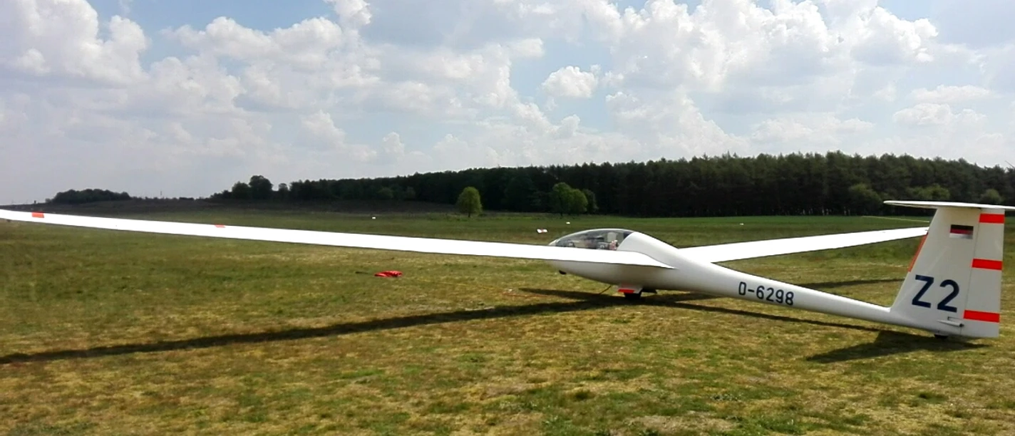 Segelfluggelände des Luftsportvereins Papenburg-Hümmling e.V. Segelflugzeug mit ausgebreiteten Flügeln auf einer grünen Wiese unter leicht bewölktem Himmel.