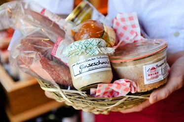 schinkendiele-wurst-praesentkorb Jemand hält einen Präsentkorb mit Ammerländer Wurst, Gänseschmalz und kariertem Tuch.