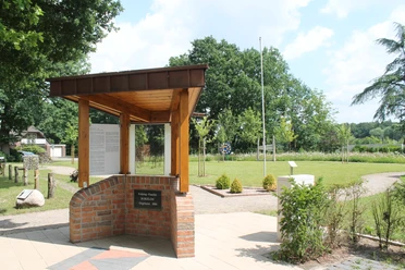 Kolpingwiese Bokeloh Grünfläche mit Pavillon aus Holz und Backstein, Informationstafel und umgebenden Bäumen.