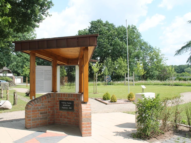 Kolpingwiese Bokeloh Grünfläche mit Pavillon aus Holz und Backstein, Informationstafel und umgebenden Bäumen.