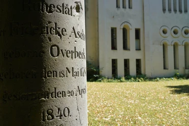 alter Grabstein mit unleserlicher Inschrift auf Friedhofswall