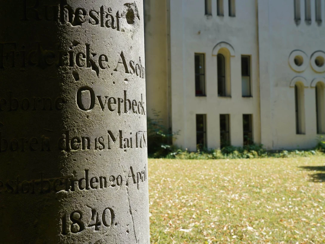 alter Grabstein mit unleserlicher Inschrift auf Friedhofswall