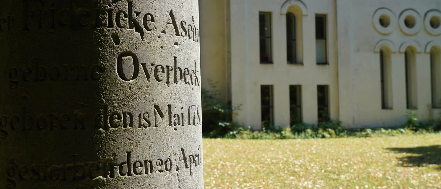 alter Grabstein mit unleserlicher Inschrift auf Friedhofswall