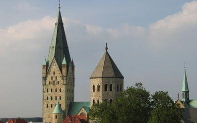 Zwei gotische Kirchtürme erheben sich eindrucksvoll gegen einen blauen Himmel, umgeben von Bäumen.
