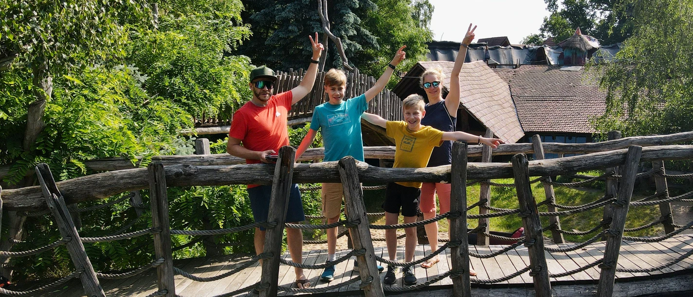 Kulturinsel Einsiedel©Fravely (10).jpeg Vier Personen stehen fröhlich auf einer Holzbrücke in einem grünen Parkgebiet.