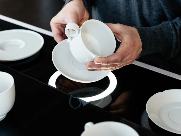 Hände, die weiße Tasse und Untere in der Hand halten, vor schwarzem Grund