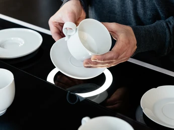 museum-schloss-fuerstenberg-anfassenerlaubt Hände, die weiße Tasse und Untere in der Hand halten, vor schwarzem Grund