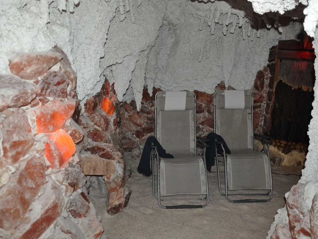 sitzplaetze-salzgrotte Eine Salzgrotte mit zwei Liegestühlen, umgeben von salzbedeckten Wänden und gedämpfter Beleuchtung.